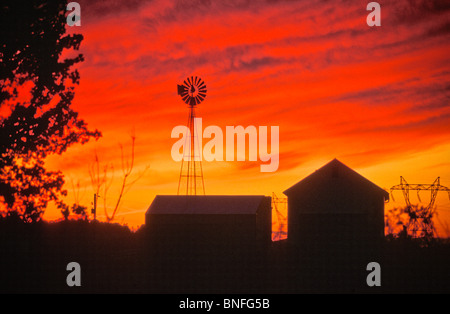 bewölktem Himmel leuchtend rote Sonnenuntergang Windmühle Bauernhof Gebäude Scheunen Stromleitungen kopieren Raum Stockfoto