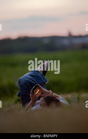 Kleiner Junge ein Video-Spiel auf dem iPhone, im Freien, im Gras von einem Bauernhof in North Carolina, USA. Stockfoto