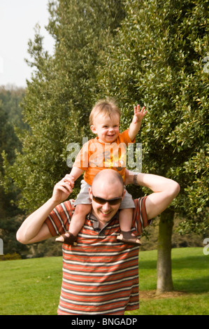 Vertikale Porträt eines jungen Vaters mit seinem Sohn auf seinen Schultern in der Sonne. Stockfoto