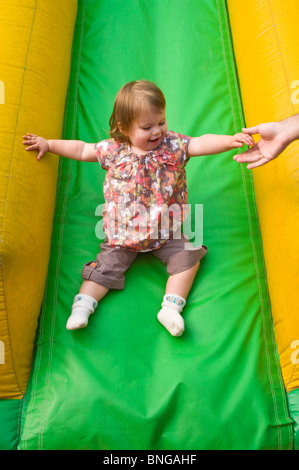 Vertikale Porträt eines Mädchens mit viel Spaß eine inflatible Folie mit einer helfenden Hand an einem soft-Play-Bereich abrutschen. Stockfoto