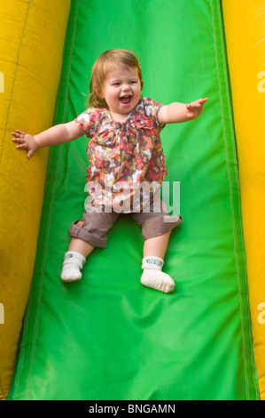 Vertikale Porträt eines Mädchens mit viel Spaß eine inflatible Folie auf eine weiche Spielplatz rutschen. Stockfoto