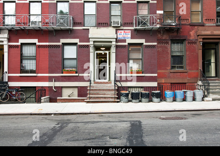 typische Folge der alten Rechtsprechung Mietskasernen in Hells Kitchen mit Mülltonnen aufgereiht auf Bürgersteig in ordentlich recycling Reihenfolge NYC Stockfoto