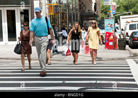 Fußgänger, darunter zwei hübsche Freundinnen in Sommerkleidern identisch Einkaufstaschen tragen überqueren 57th Street New York City Stockfoto