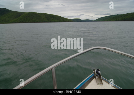 Motion Blur in den unteren Bereichen Wasser mit über cast Himmel oben. Hohe Winkel einer Boote Bug von Wasser umgeben. Zwei Stücke von Land durch eine Staumauer verbunden. Stockfoto