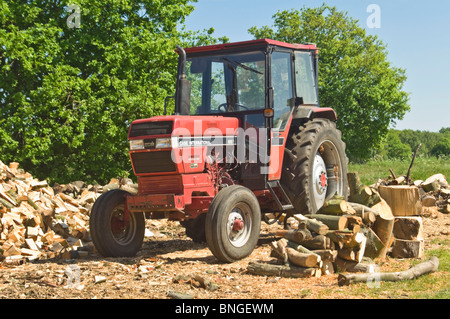 Horizontale Nahaufnahme von leuchtend roten Fall International Traktor durch einen großen Holzstapel in der Sonne abgestellt. Stockfoto