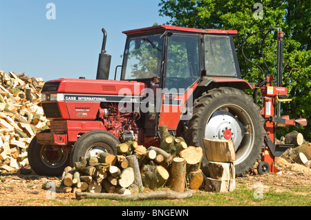 Horizontale Nahaufnahme von leuchtend roten Fall International Traktor durch einen großen Holzstapel in der Sonne abgestellt. Stockfoto