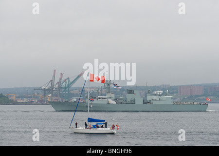 Ein Segelboot, das Ahornblatt fliegen geht vor HMCS ST. JOHN es während der 2010 Fleet Review in Halifax, Nova Scotia. Stockfoto