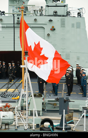 Die Ahornblatt-Flagge fliegt aus dem Achterdeck der HMCS ST. JOHN es während die Besatzung stramm im Hintergrund steht. Stockfoto