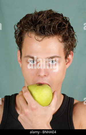 Junger Mann beißt einen Granny Smith Apfel auf einem grünen Hintergrund. Konzept für eine gesunde Ernährung. Stockfoto