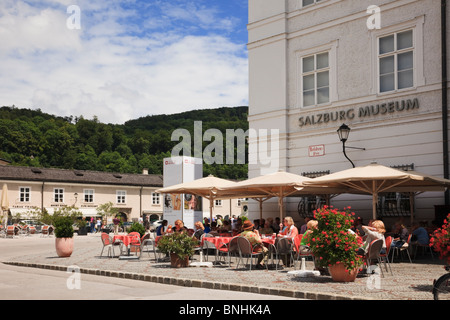 Residenzplatz, Salzburg, Österreich. Menschen Essen im Straßencafé vor Salzburg Museum mit Mozart-Statue über Stockfoto