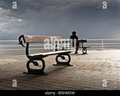 Ein Mann sitzt allein auf einer Bank an der Promenade, grau bedeckt Juli Sommernachmittag, Aberystwyth Wales UK Stockfoto