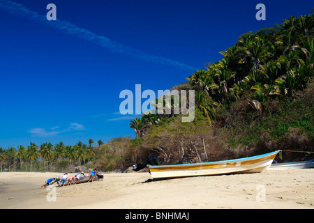 Ein Fischer schiebt sein Boot wieder am Strand mit Hilfe seiner Familie. San Pancho, Bundesstaat Nayarit, Mexiko Pazifikküste. Stockfoto