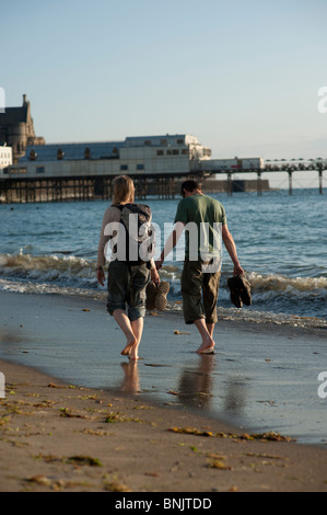 Rückansicht eines jungen Paares, zu Fuß entlang des Strandes an der Aberystwyth Wales Großbritannien an einem Sommerabend Stockfoto