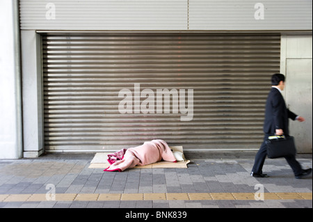 Obdachloser schlafen rau in Shinjuku, während Mann vorbei, Tokyo, Japan geht Stockfoto