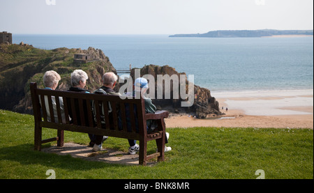 Vier ältere Menschen sitzen in der Sonne auf der Bank am Meer Tenby Wales UK Stockfoto