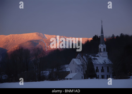 Eine Kirche sitzt im Vordergrund in Waitsfield, VT, wie Sugarbush Resort Mt. Ellen Gnade Hintergrund in Fayston, VT Routen Stockfoto