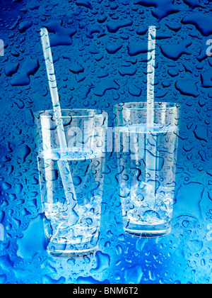 Zwei Gläser Wasser mit Trinkhalme mit Wassertropfen auf blauem Hintergrund Stockfoto