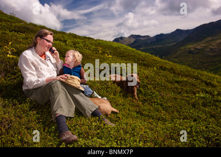 Mutter und Tochter sitzen auf einem Hügel sprechen auf einem Handy, Hatcher Pass, Alaska Stockfoto