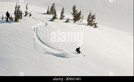 Ein Skifahrer und Snowboarder beobachten, wie ein Kerl Backcountry Skifahrer einen Abstieg in Turnagain Pass, Alaska beginnt Stockfoto