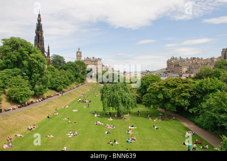 Menschen genießen die Sonne in Princes Street Gardens, Edinburgh, mit Scott Monument im Hintergrund. Stockfoto