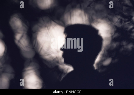 Kopf eines jungen Mannes im Profil, Schatten weich gegen eine Wand in gefleckten Licht mit dem Schatten von Sträuchern und Pflanzen. Stockfoto