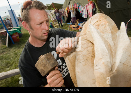 Glastonbury Festival. Bildhauer im Bereich Green Fields des Festivals auf eine hölzerne Skulptur arbeiten. Stockfoto
