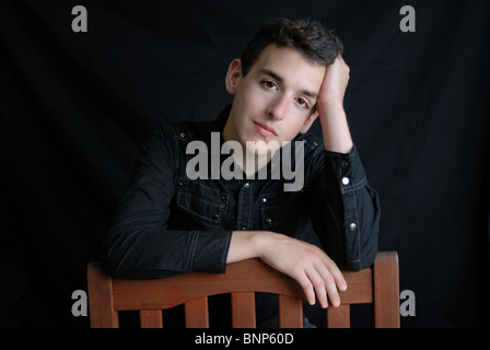 Porträt eines jungen Mannes mit dunklem Haar sitzt auf einem Stuhl gestellt. Stockfoto
