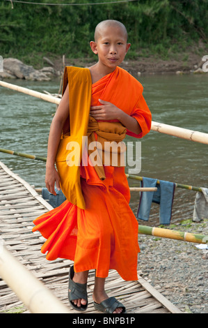 Ein junger Mönch geht über eine Bambusbrücke in Luang Prabang Laos Stockfoto