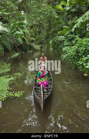 Mann Rudern Indien Tourist Frau mit hell lila und grüne Sari auf ein hölzernes Kanu entlang der schönen malerischen Stauwasser Kanäle Stockfoto