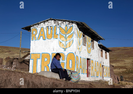 Mädchen sitzt auf einem Felsen vor dem Haus mit Propaganda für die Kandidatin der Weizenpartei für Kommunalwahlen gemalt, in der Nähe von Yanaoca, Cusco Region, Peru Stockfoto