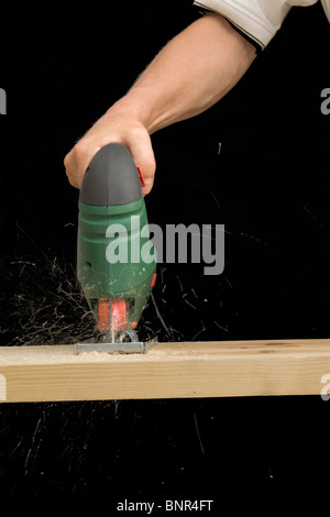 Ein Mann mit einem elektrischen Stichsäge ein Brett aus Holz zu schneiden Stockfoto