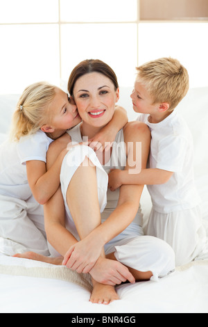 Kinder küssen ihre Mutter sitzt auf einem Bett Stockfoto
