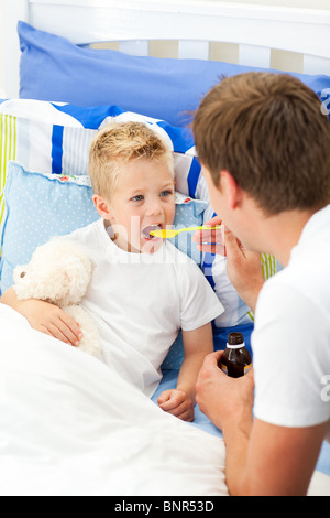 Liebevoller Vater seinen kranken Sohn Hustensaft geben Stockfoto