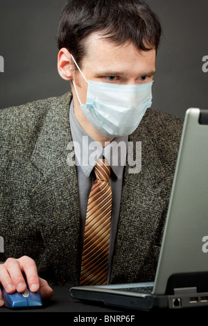 Ein Mann in einer medizinischen Maske arbeitet mit dem laptop Stockfoto