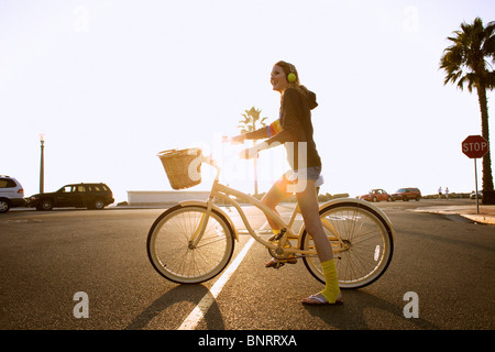 Junge Frau trägt ein Kopfhörer, gelben Socken und ein Hoodie reitet ein Cruiser-Fahrrad zum Strand. Stockfoto