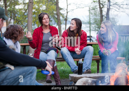 Eine Gruppe von Freunden sitzen und genießen Sie Getränke während des Gesprächs ein Lagerfeuer. Stockfoto
