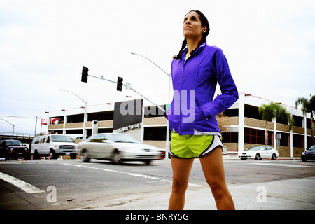 Ein weibliche Läufer steht an der Ecke zweier Straßen und Autos vorbei im Hintergrund erstellen Motion blur in San Diego. Stockfoto