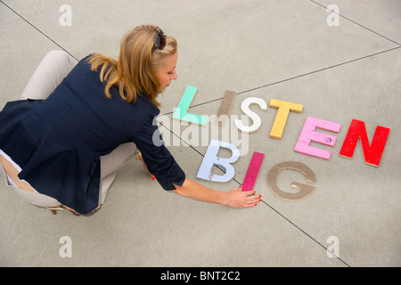 Attraktive blonde Frau posiert neben den Satz "Big hören" ausgeschrieben in Druckbuchstaben auf dem Boden neben ihr Stockfoto