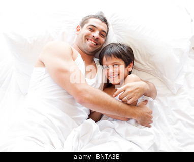 Vater und Sohn auf dem Bett in die Kamera schaut lächelnd Stockfoto