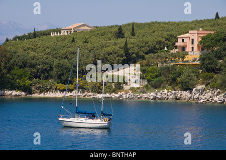 Luxus-Villen am bewaldeten Hang mit Segelyacht vor Anker in der Bucht bei Kassiopi auf der griechischen Mittelmeer Insel Korfu Griechenland Stockfoto