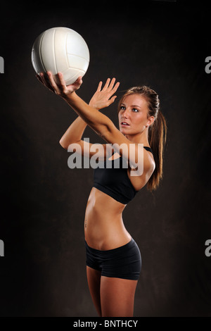Schöne junge Frau, die auf dunklem Hintergrund Volleyball spielen Stockfoto