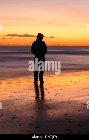 Ein Mann allein denken, Blick auf das Meer, während die Sonne untergeht. Stockfoto