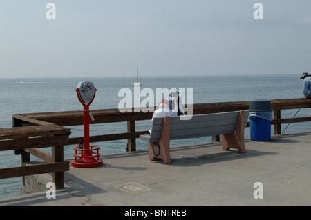 Ältere Frau genießen den Blick auf das Meer von einer Bank auf einem Pier. Stockfoto