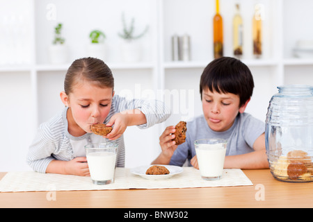 Glücklich Geschwister essen Kekse und Milch trinken Stockfoto