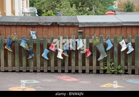 Einen bunten Garten gemacht aus einer Reihe von sortierten Gummistiefel an einem Zaun auf dem Spielplatz der Symondsbury Primary School. Stockfoto
