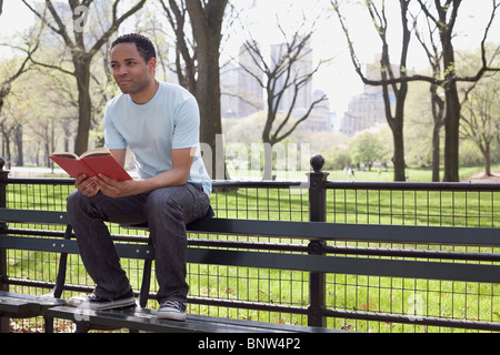 Mann sitzt auf der Bank Lesebuch im Central Park Stockfoto
