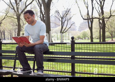 Mann sitzt auf der Bank Lesebuch im Central Park Stockfoto