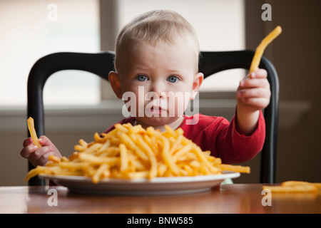 Kleinkind Essen einen großen Teller mit Pommes frites Stockfoto