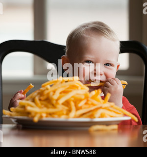 Kleinkind Essen einen großen Teller mit Pommes frites Stockfoto