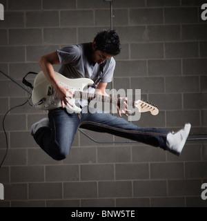 Mann springt in die Luft beim Gitarre spielen Stockfoto